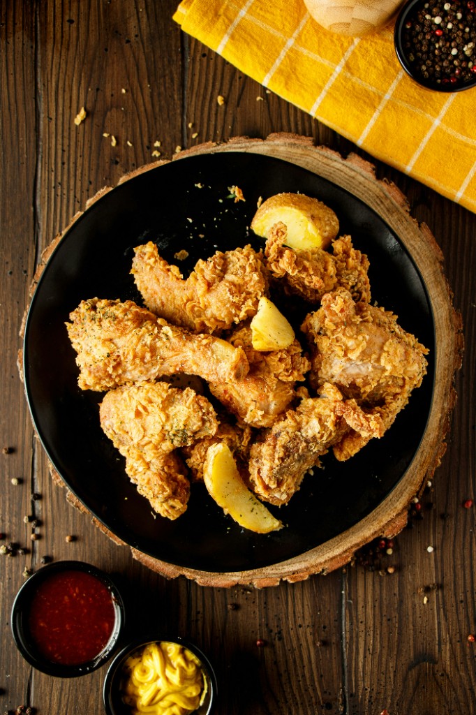Fried chicken and potato wedges on a black plate with dipping sauces