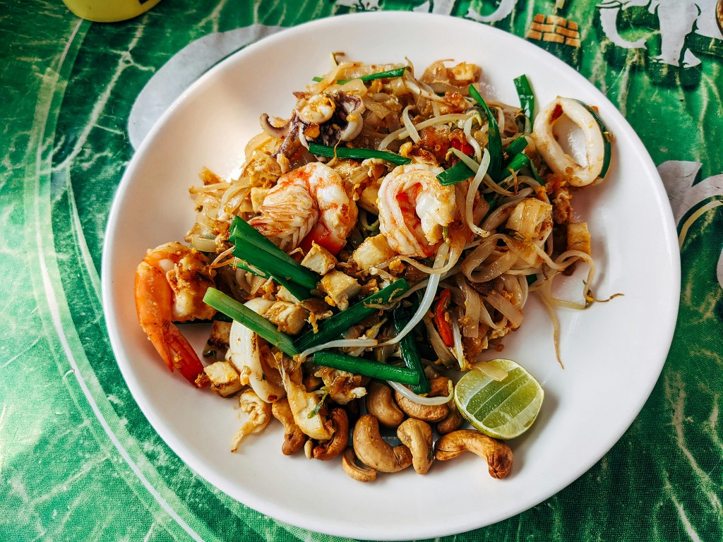 Seafood pad thai with shrimp, noodles, and garnishes on a white plate